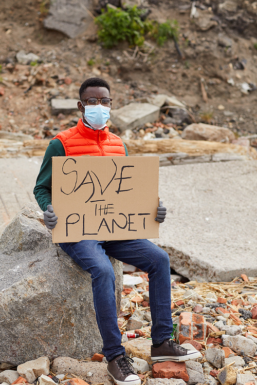 Portrait of African young volunteer sitting on the stone holding placard and looking at camera outdoors