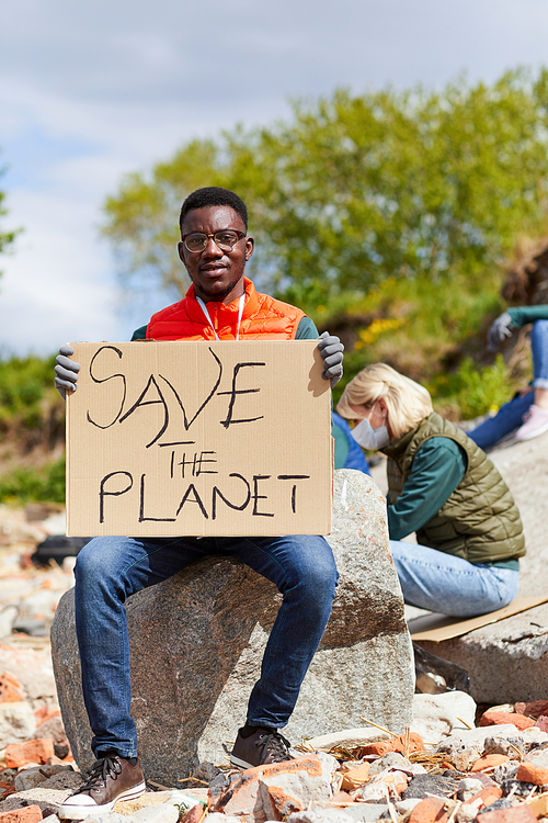Portrait of African young man holding placard and looking at camera while sitting on the stone outdoors