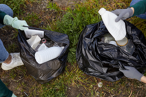 Close-up of people in protective gloves putting garbage from the ground into the garbage bags outdoors