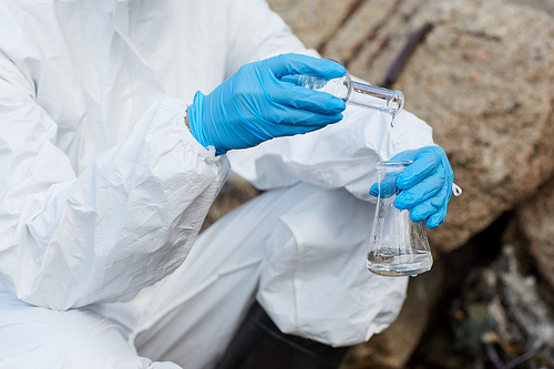 Close-up of woman in protective gloves and suit holding flasks and taking samples of water