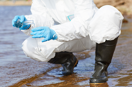 Close-up of chemist in protective workwear and in gloves holding flask and examining the water in the river