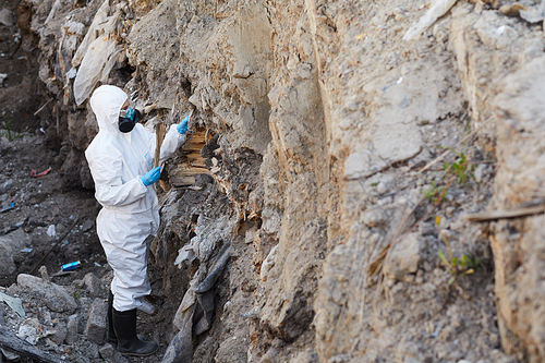 Ecologist in protective suit examining the samples of rocks in the nature