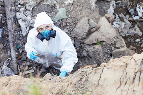 Portrait of young ecologist in protective suit looking at camera while examining the rocks