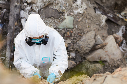 High angle view of biologist in protective suit taking samples of rocks outdoors