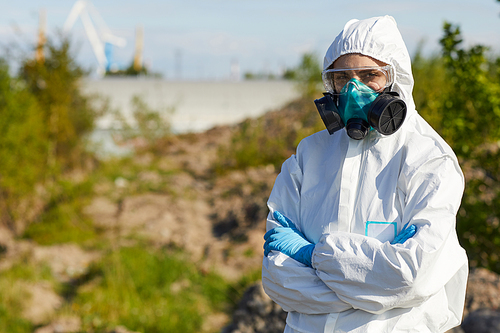 Portrait of young woman in protective workwear and mask standing with arms crossed and looking at camera she working in dangerous area