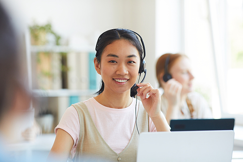 Portrait of Asian operator in headset smiling at camera while working in call center