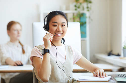 Asian call center agent wearing headset smiling at camera she working in customer support