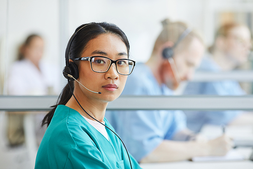 Portrait of Asian medical customer service operator in headset looking at camera during her work