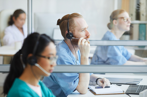 Group of operators in headphones sitting at their workplaces and working in medical call center