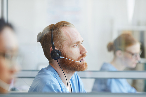 Young bearded man in headphones working in medical call center