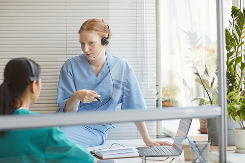 Two colleagues in headphones talking to each other during their work in medical call center