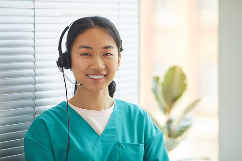 Portrait of young Asian operator in headphones smiling at camera while standing at office