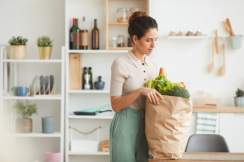 Young woman standing in the kitchen and buying the food in paper bag