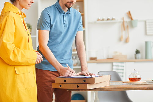 Close-up of young man signing the form for pizza while woman delivering the pizza to home