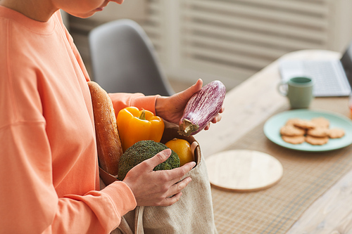 Close-up of young woman taking out the fresh vegetables from paper bag in the kitchen