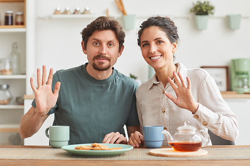 Portrait of young happy couple having breakfast and smiling at camera while sitting at the table in the kitchen