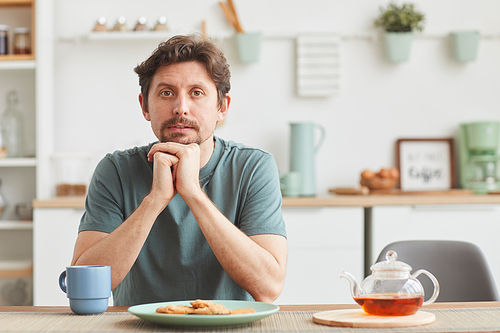 Portrait of young man sitting at the table and looking at camera during his breakfast at home
