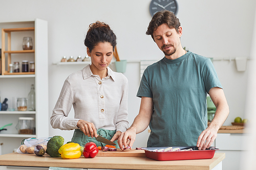 Young couple standing at the kitchen table and preparing dinner together in the kitchen at home