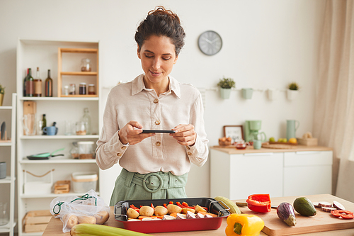Young woman photographing her special dish using her mobile phone while standing in the kitchen