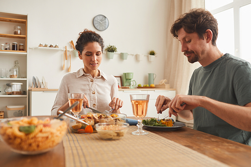 Young couple sitting at the table and enjoying dinner together in domestic kitchen