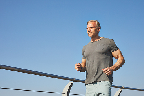 Below view of content active mature man in gray tshirt bending arms and running outdoors