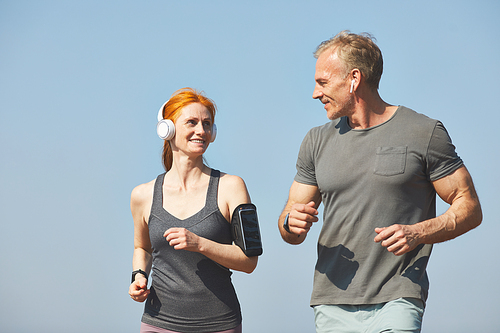 Smiling attractive redhead woman with armband enjoying jogging with boyfriend in morning