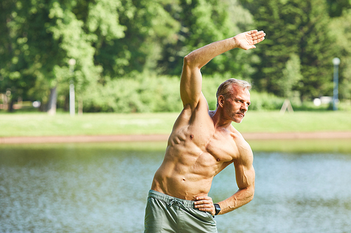 Purposeful mature man with perfect body doing warm-up exercise while training in park