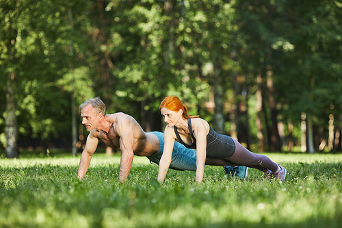 Athletic mature couple doing push-ups on grass while training together in park