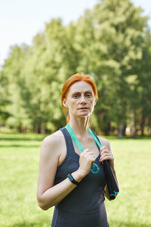 Portrait of serious fit mature woman holding jump rope around neck in beautiful park, fitness outside