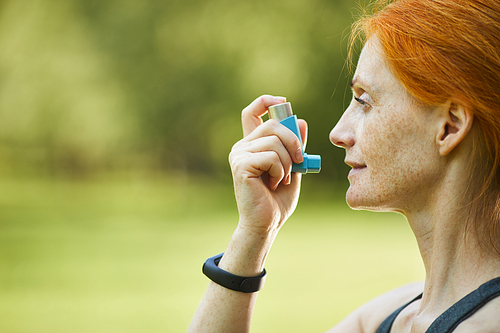 Side view of ill redhead mature woman with freckles using inhaler outside after fitness training