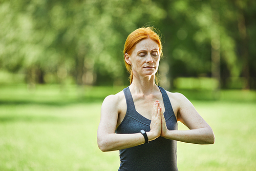 Mature redhead yogis focused on meditation standing with hands in Namaste in empty park