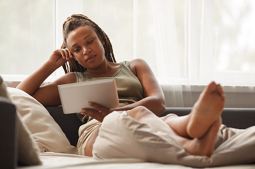 Young woman watching movie on digital tablet while relaxing on sofa on weekends