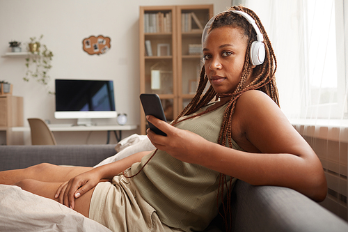 Portrait of young woman in wireless headphones using her mobile phone to listen to music she sitting at home
