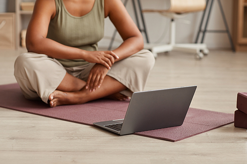 Close-up of woman sitting on exercise mat in front of laptop and watching yoga exercises online at home