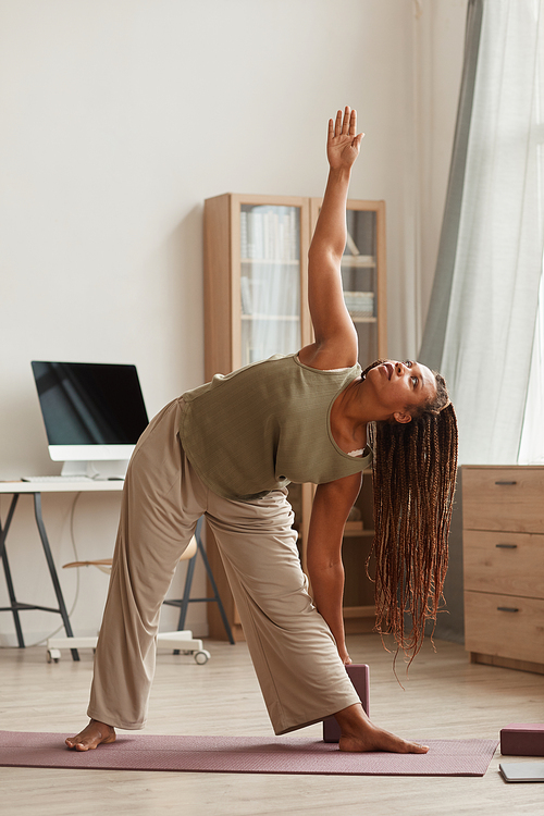 African beautiful woman standing on exercise mat and doing stretching exercises in the living room at home