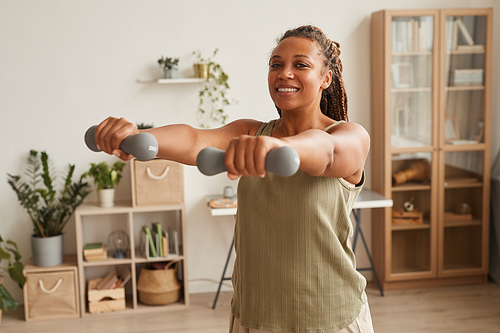 Young smiling woman standing and exercising dumbbells in the room at home
