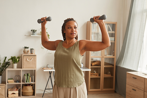 Young healthy woman raising her hands and training with dumbbells in the living room