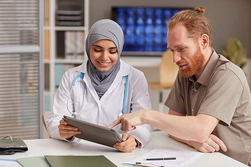 Female doctor showing medical prescription on digital tablet to her patient during his visit at hospital