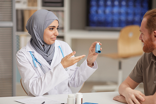 Female doctor in hijab recommending medical equipment from asthma to male patient while they sitting at hospital