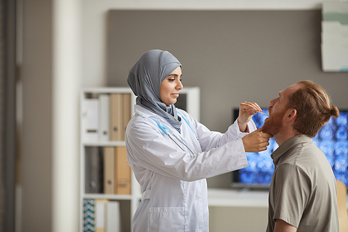 Muslim female doctor in white coat examining the throat of the patient during medical exam at hospital