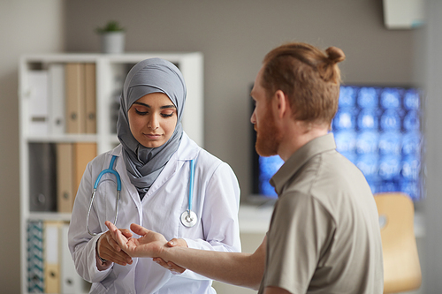Nurse in hijab examining the pulse of patient during medical exam while he visiting the doctor's office