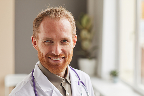 Close-up of bearded successful medical worker in white coat smiling at camera