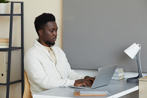 African young man sitting at the table concentrating on his online work he typing on laptop at office