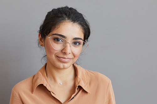 Portrait of young beautiful woman in eyeglasses looking at camera isolated on grey background