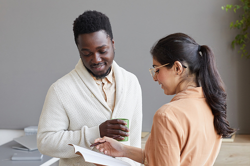 Young secretary pointing at documents and discussing them with African businessman at office