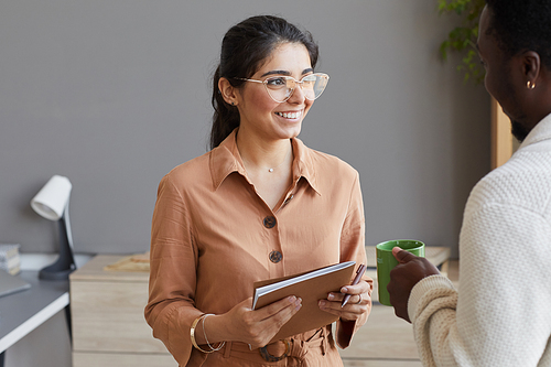 Young secretary with note pad smiling and talking to African businessman while they standing at office