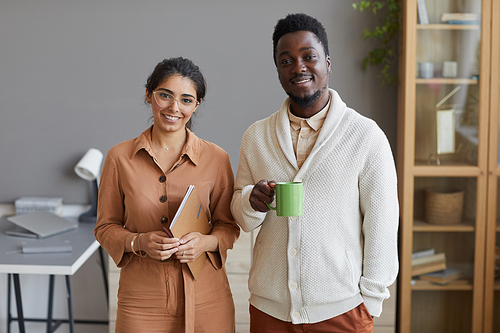 Portrait of young successful business people smiling at camera while standing together at office