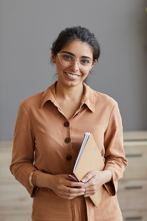 Portrait of young successful businesswoman in eyeglasses smiling at camera while standing at office