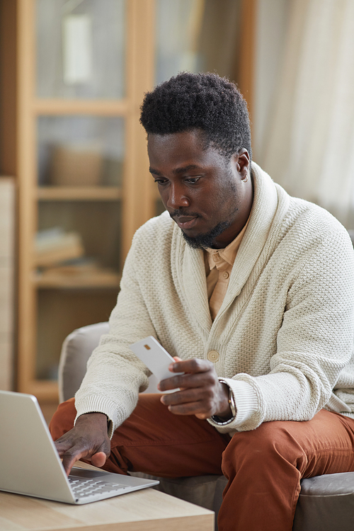 African young man sitting in front of the laptop and doing shopping online using his credit card