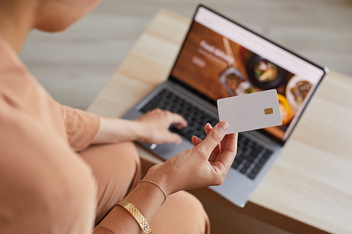 Close-up of woman sitting in front of the laptop ordering food online and paying for it with credit card